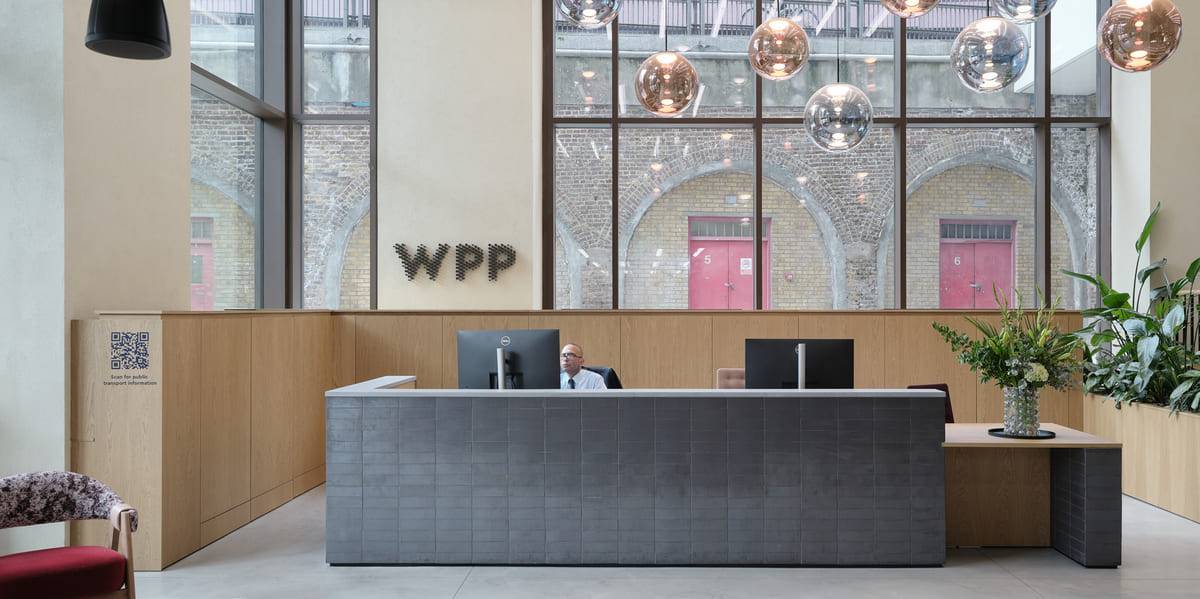 Office reception desk under a double-height glazed wall with pendant globes